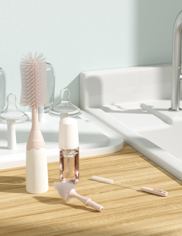 Momcozy bottle brush kit with main brush, cleaning solution, and accessories on a wooden countertop.