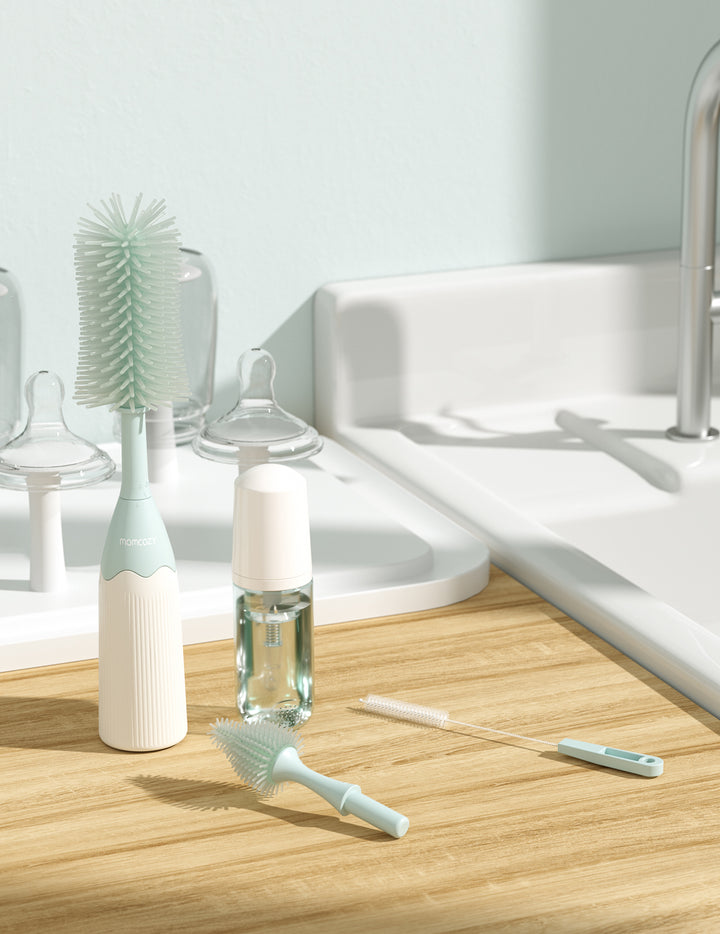 Momcozy teal bottle brush kit with cleaning solution and accessories on a wooden countertop.