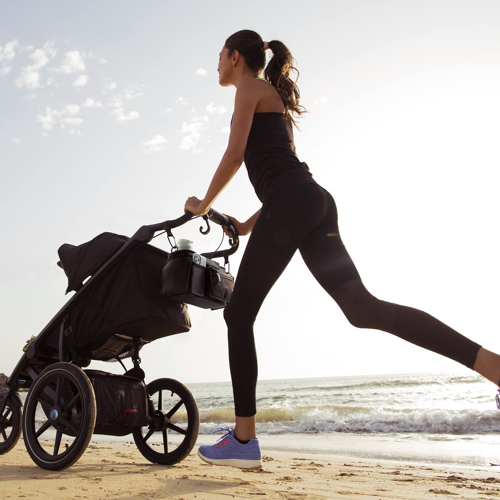 Momcozy stroller organizer attached to a stroller, with woman jogging on beach