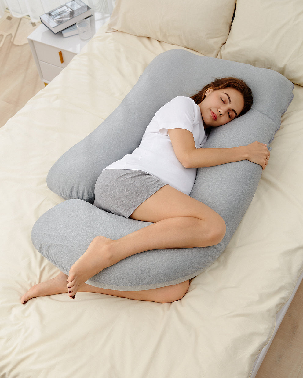 Pregnant woman sleeping on a light gray U-shaped maternity pillow, finding comfort and support in bed.